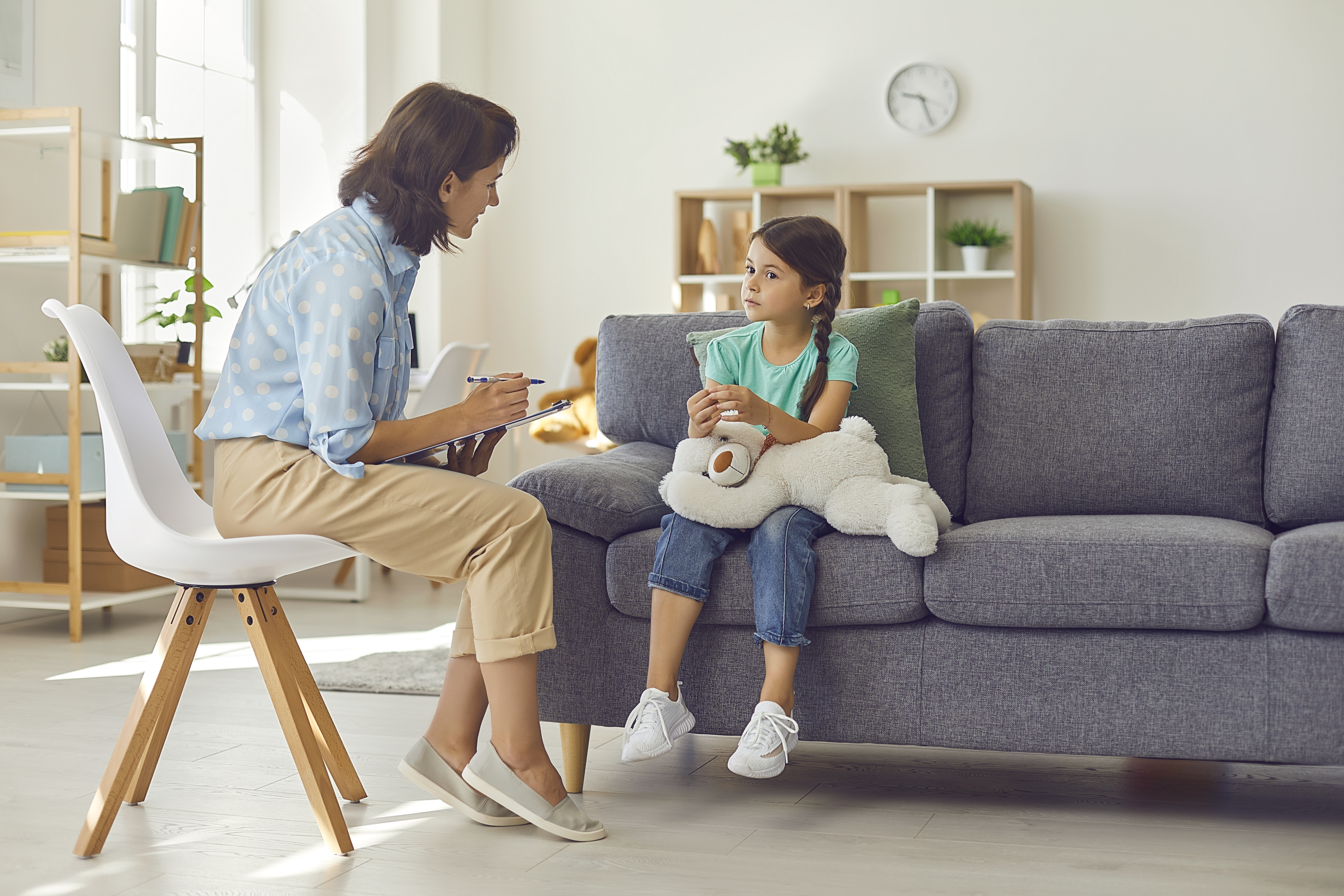 psychologist working with a preschool child in a bright office. Woman makes notes about the condition of the girl on paper