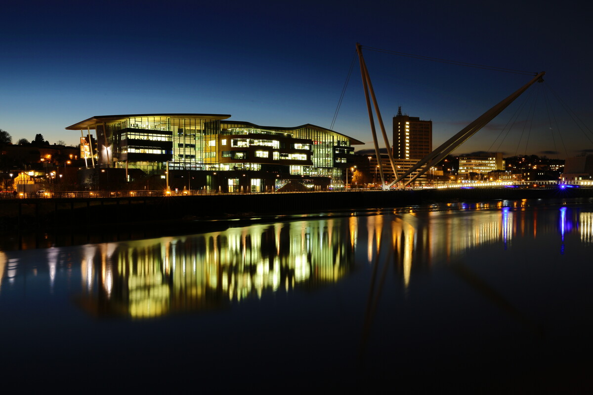 A riverside view of the Newport Campus at night.