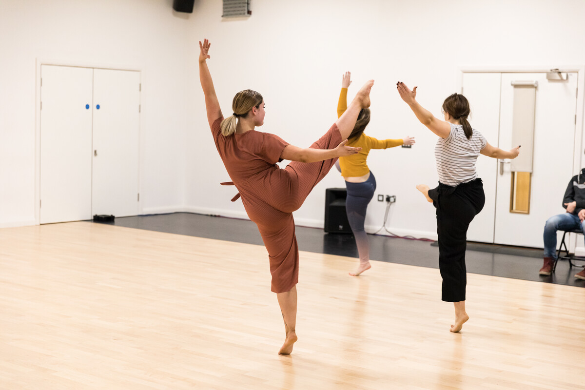 Three students dancing together on a sprung dance floor in a rehearsal studio at Cardff campus