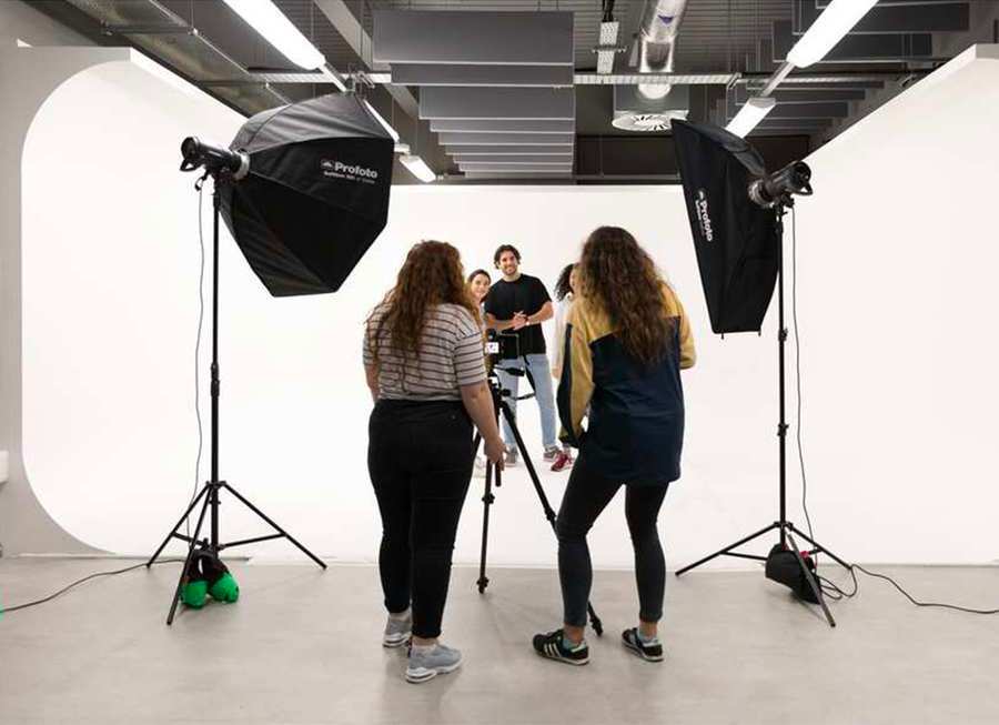 Students setting up professional lights and cameras to photograph two people stood against the white backdrop in the photography studio.