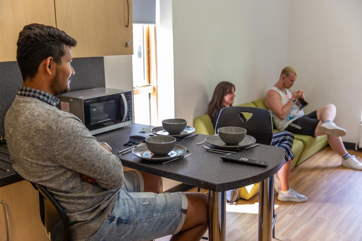 one student sitting at the breakfast bar and two students sitting on the sofa in the communal area of mountain halls in pontypridd