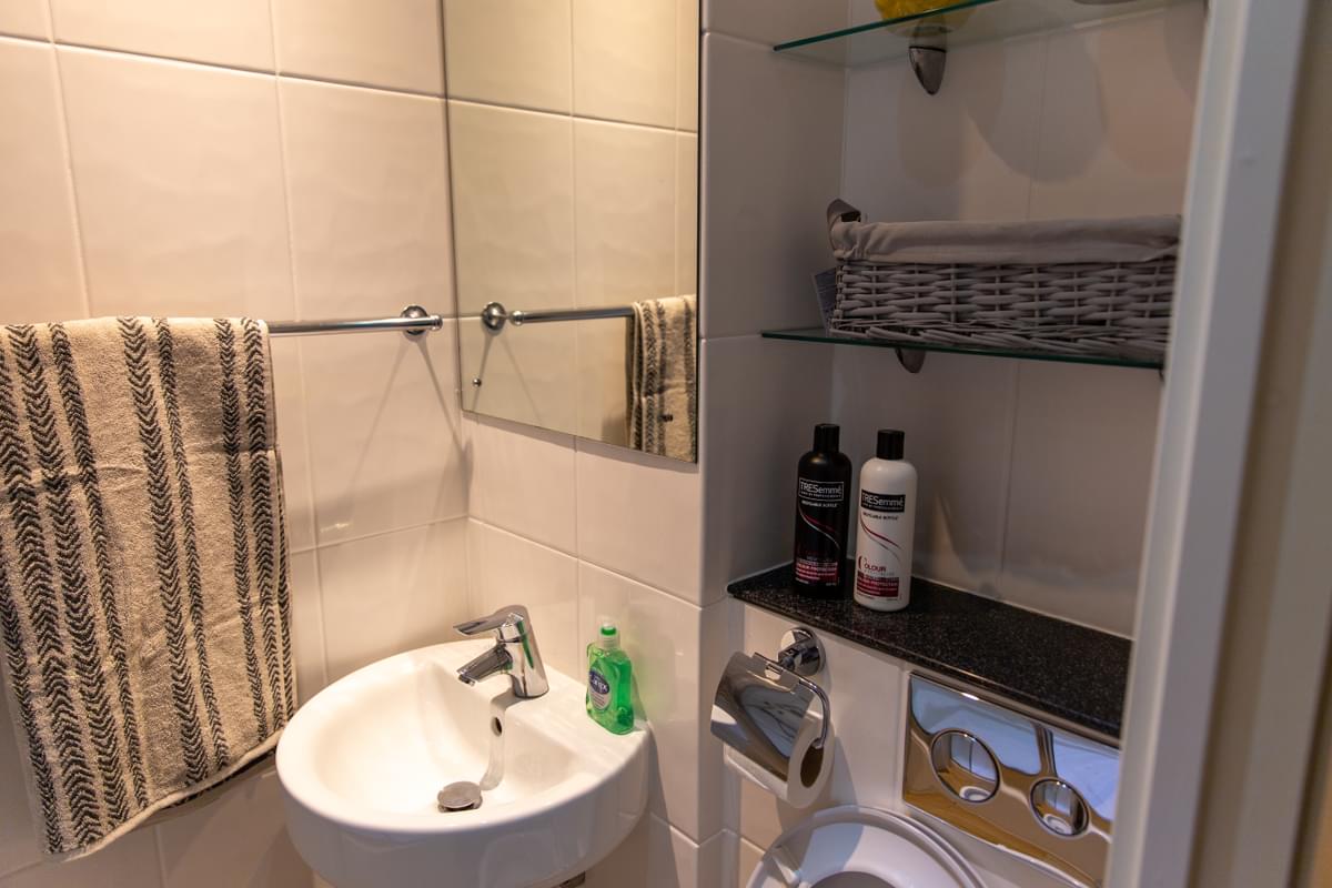 the bathroom in mountain halls pontypridd - a sink with soap, mirror, shelves, toilet and towel rail