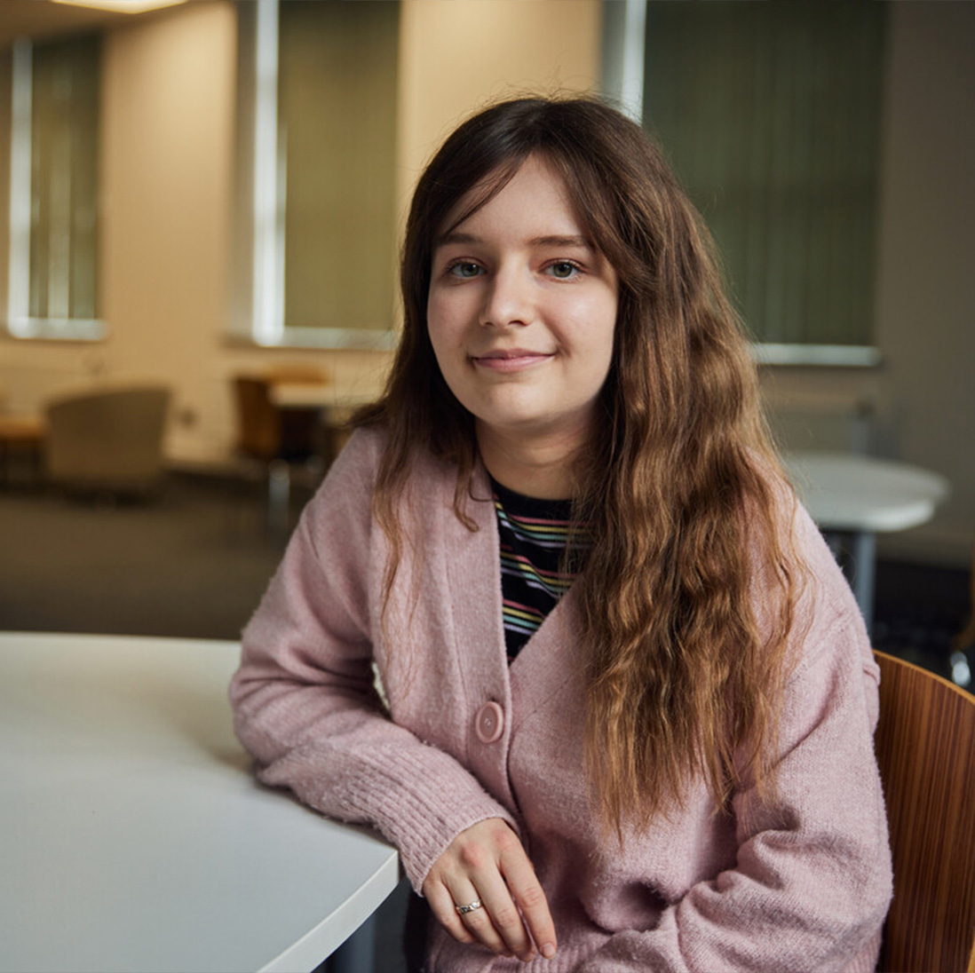 An accounting student smiles at the camera while sat at a table and leaning on their elbow from the Postgraduate Centre in Treforest