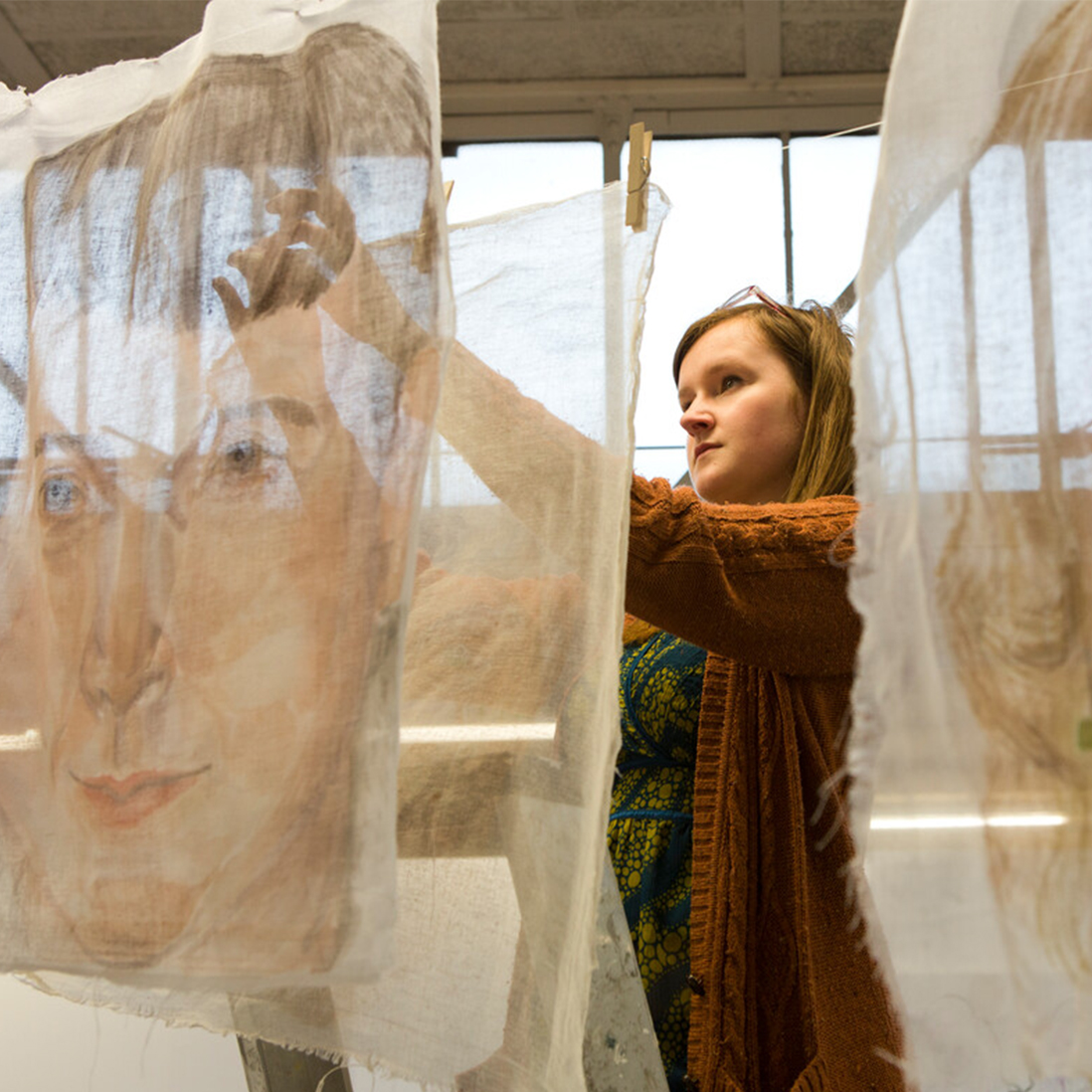 A student repositions a piece of a fabric with a face painted on it in an art workshop