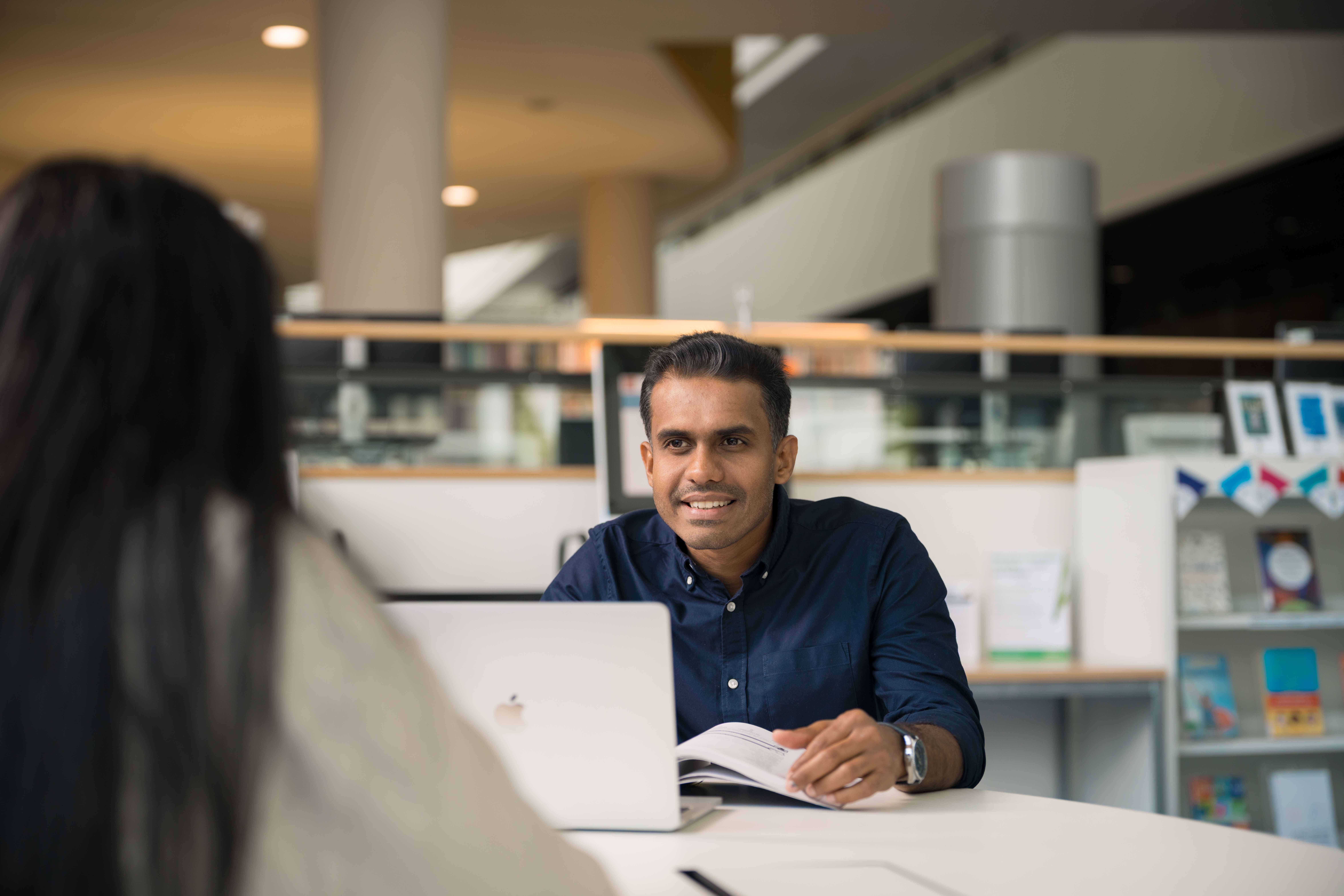 Two MBA Global students working opposite each other on a table in a library setting.