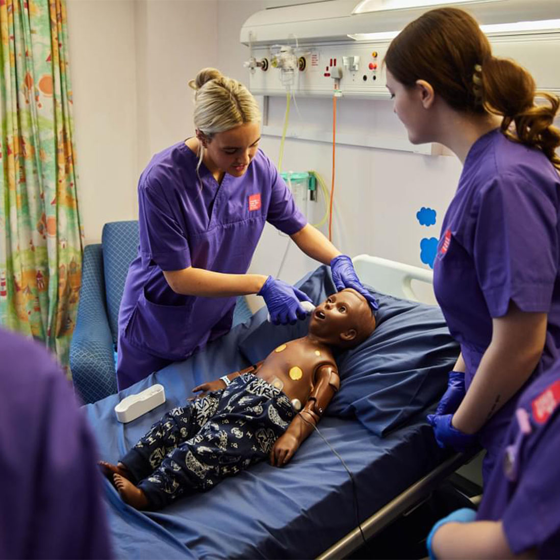 Two nursing students practicing examination techiniques on a child mannequin in the clinical simulation centre