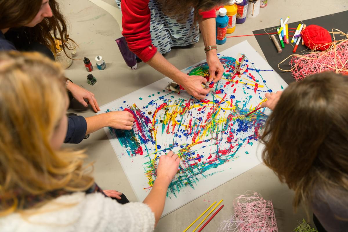 A group of students paint an abstract pattern together on one piece of paper with paints of various different colours at the USW Newport campus