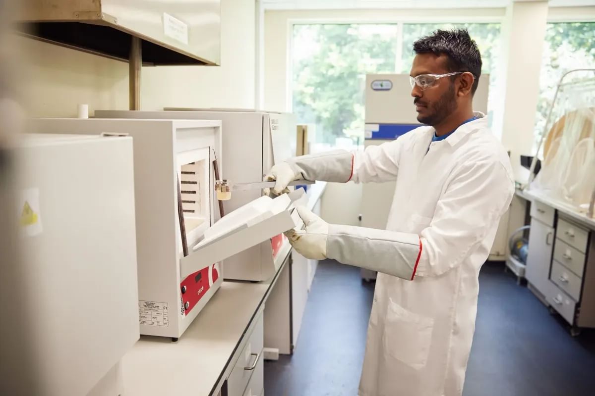 A student dressed in a white laboratory coat and gloves completes an experiment using equipment in a USW lab at the Treforest campus