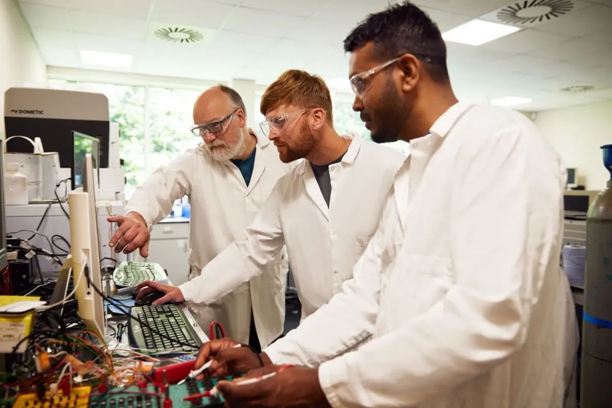 Two students and an academic, all wearing white laboratory coats, focus on an experiment inside a USW lab at Glyntaff campus