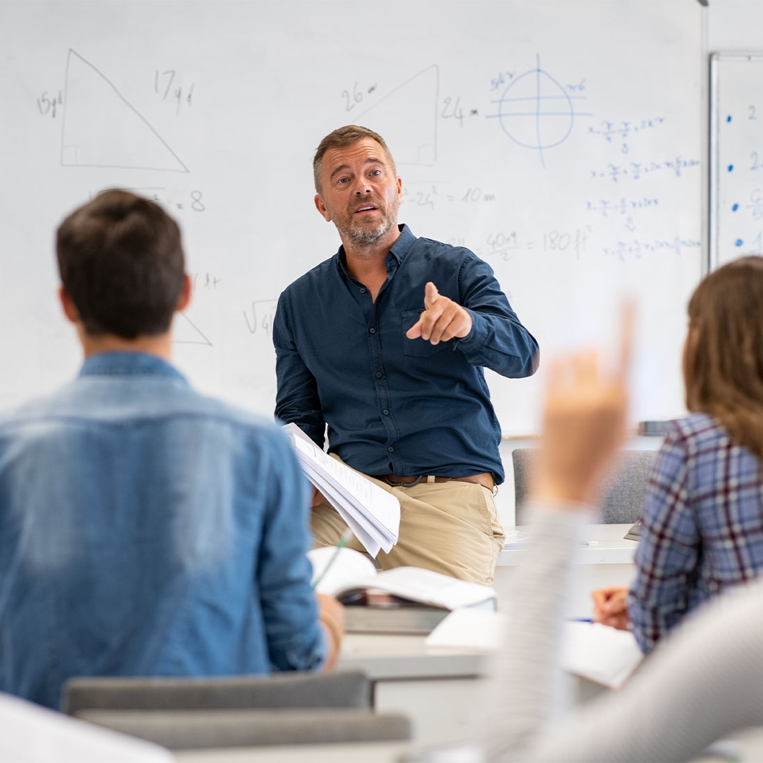 A mature teacher taking questions from pupils in a classroom