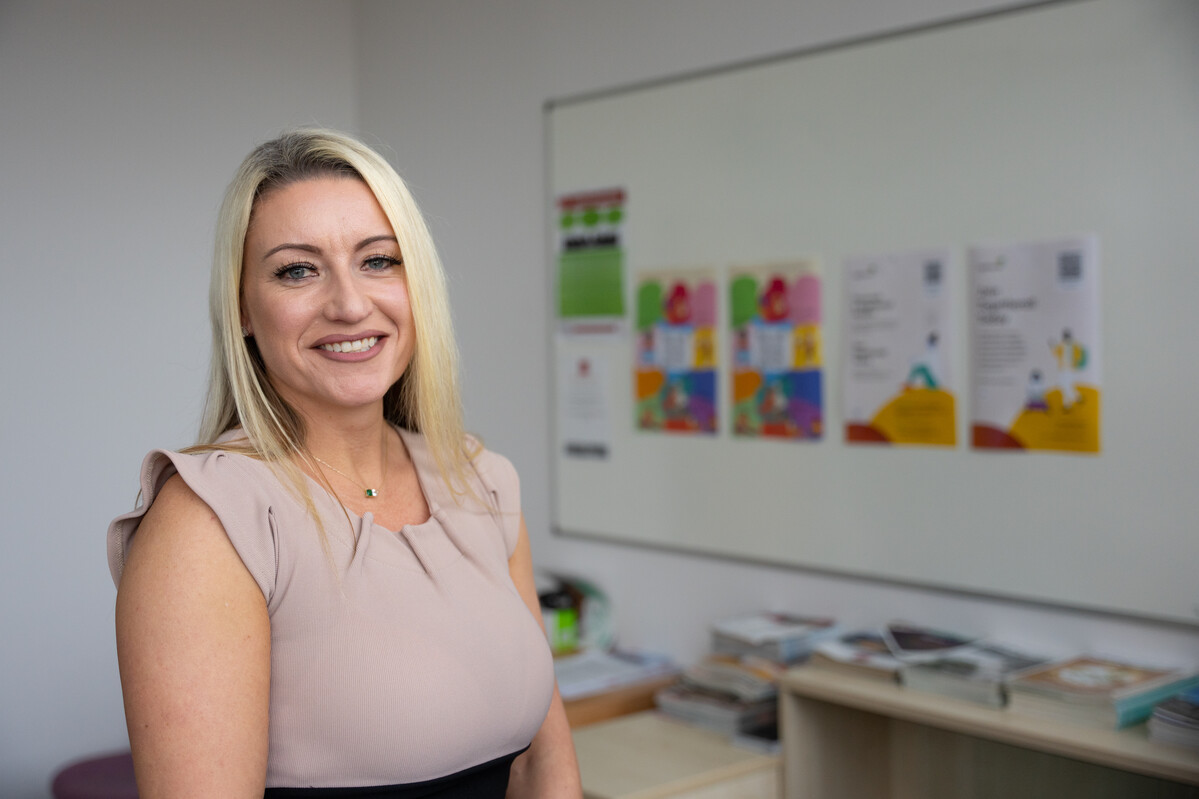 A real estate professional smiles at the camera while standing in front of a white board with posters stuck to it in an office