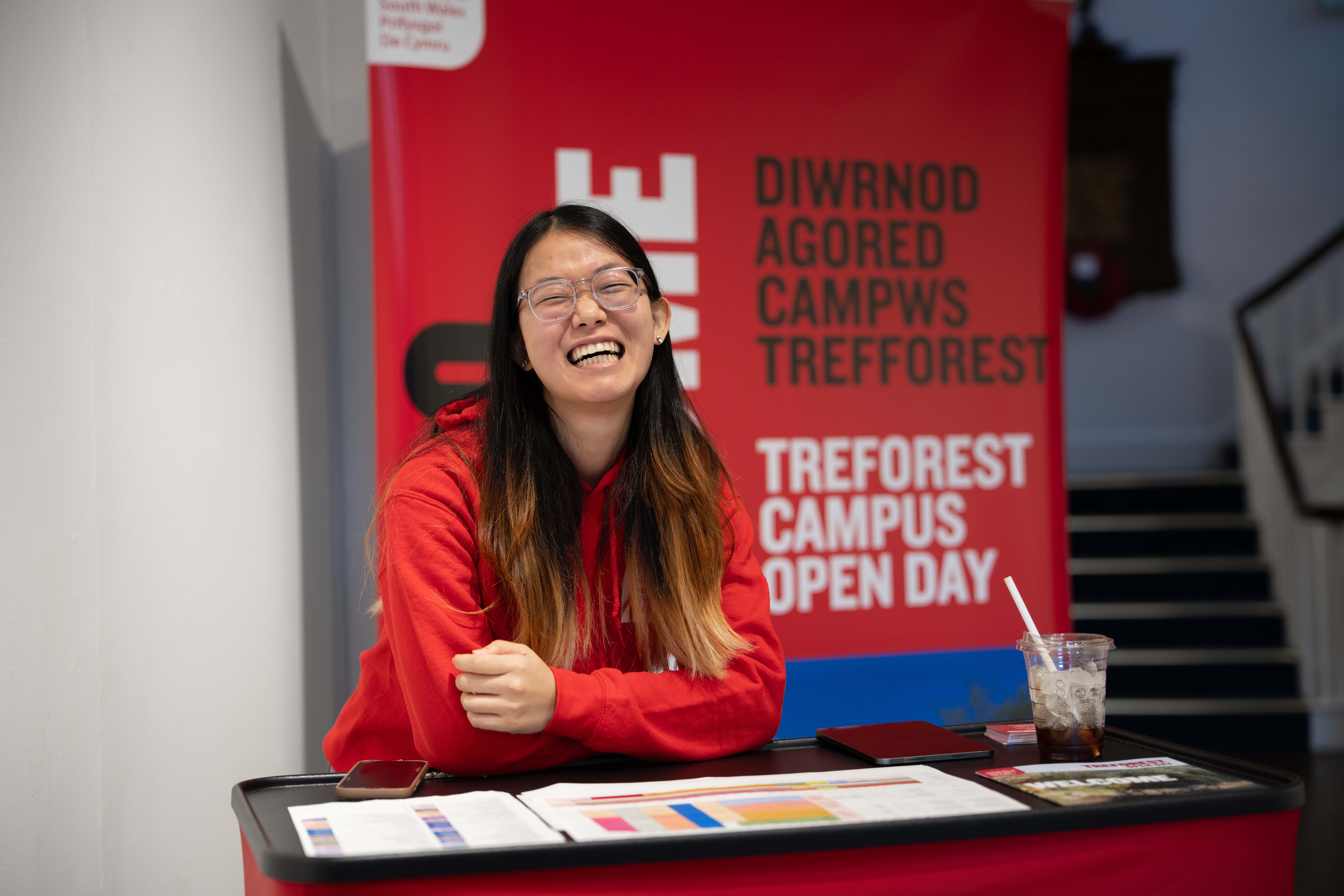 A student ambassador smiling at the camera in front of an Open Day sign.