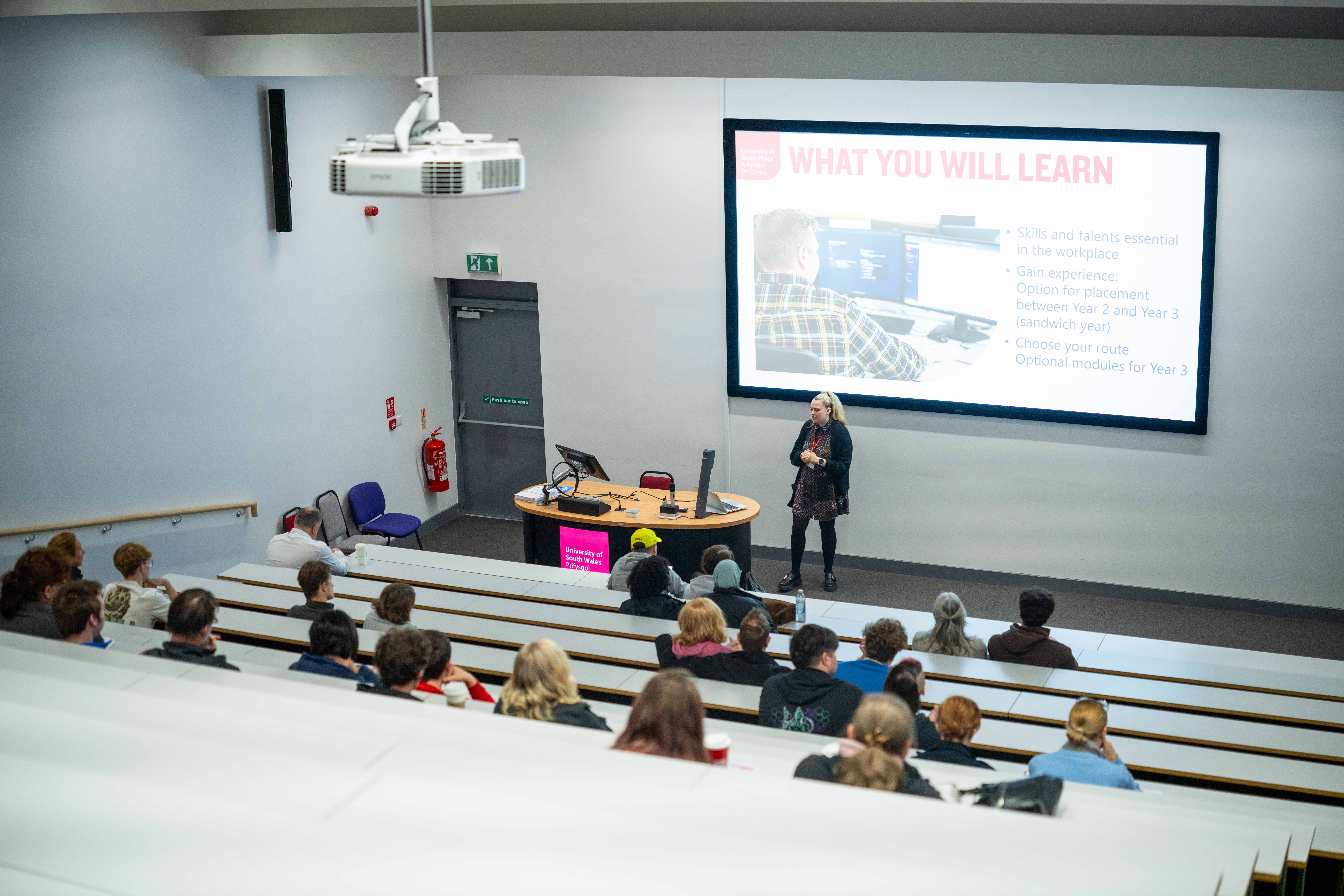 Open day visitors sat in a lecture theatre listening to a lecturer giving a talk.