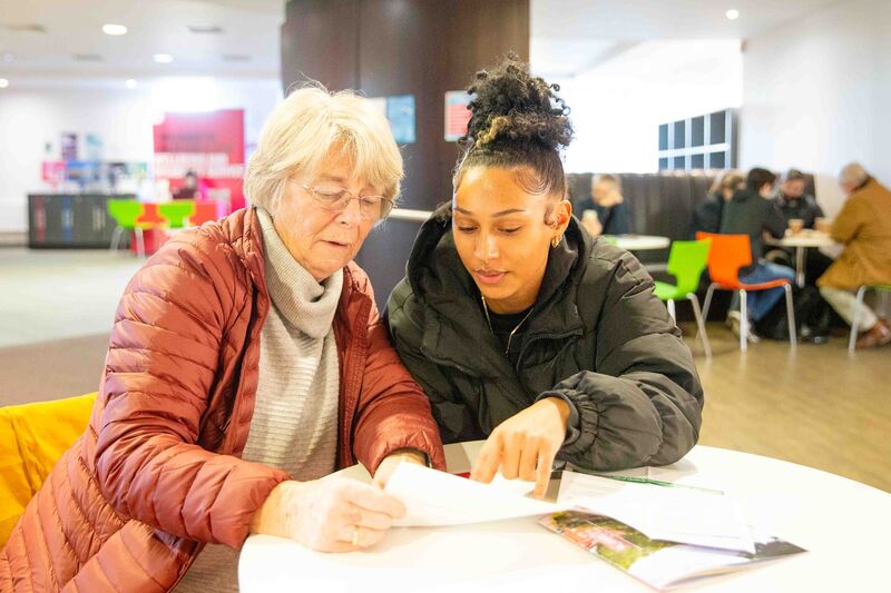 Two open day visitors are sat together at a table, looking at a programme of events.