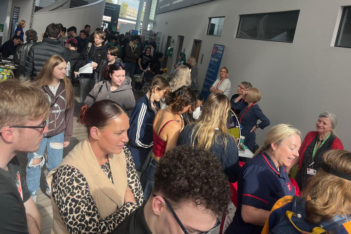 A crowd of people gathered in the Atrium, visiting multiple information stands at a welcome event