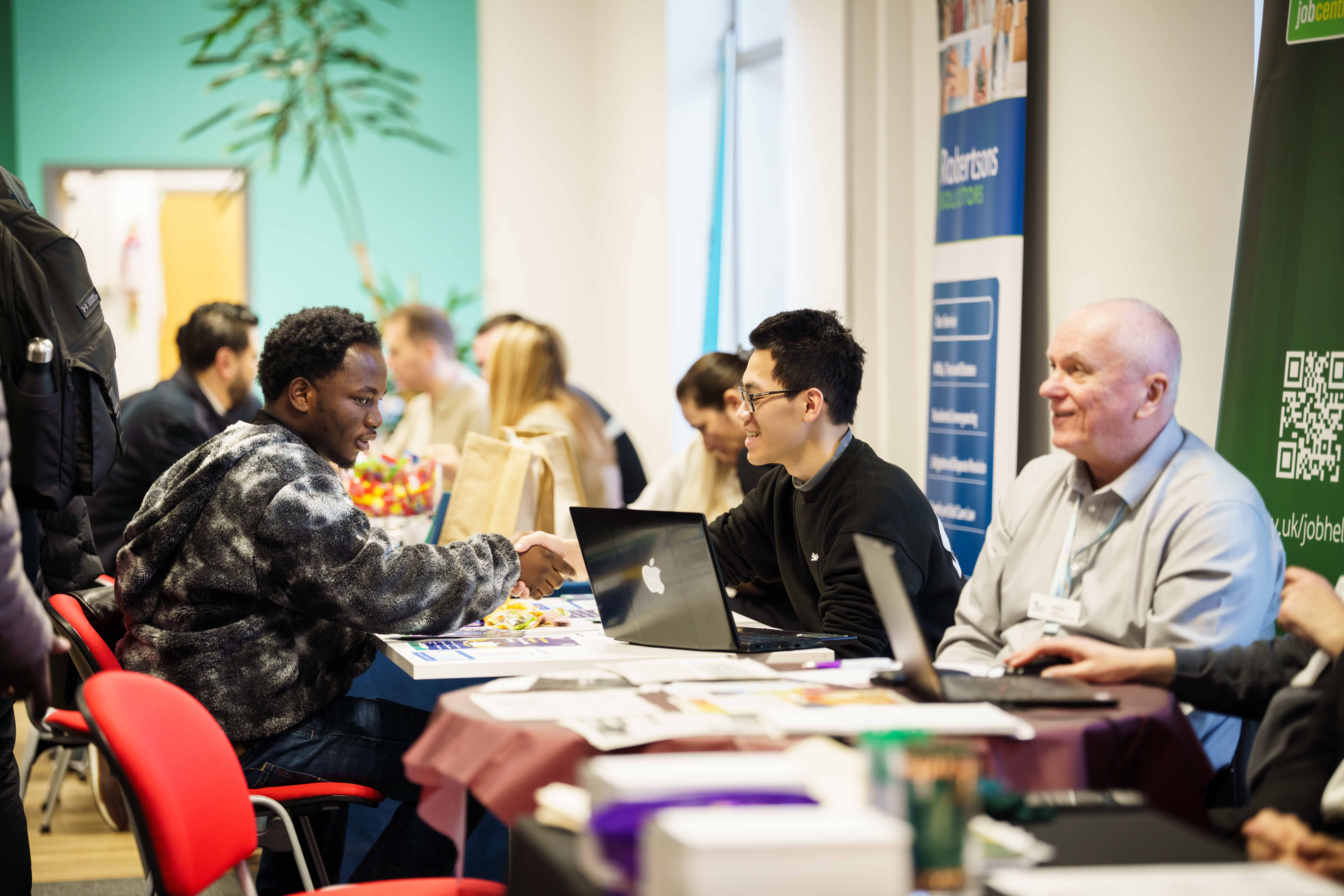 Students and employers discussing opportunities at various stalls at a graduate event.
