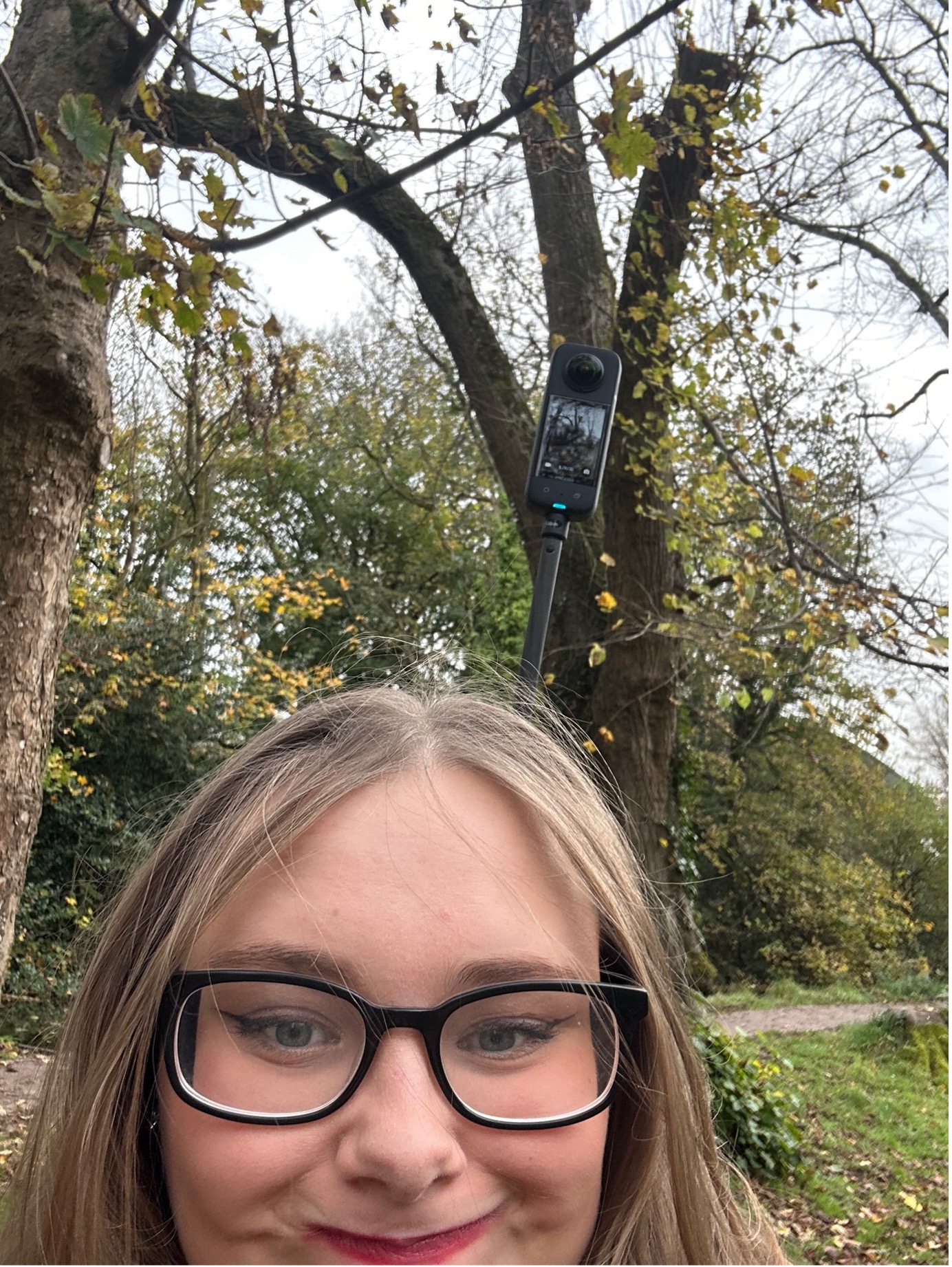 Student, Millissa, has taken a selfie with a camera behind her. There are tree's in the background.