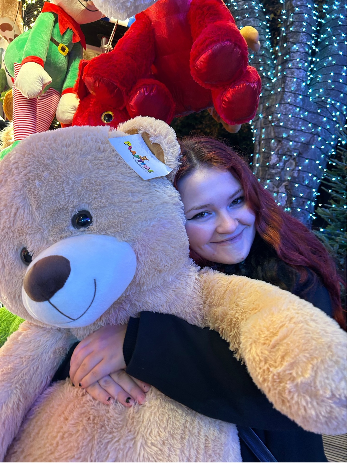 A young woman hugging a large teddy bear won at a fair.