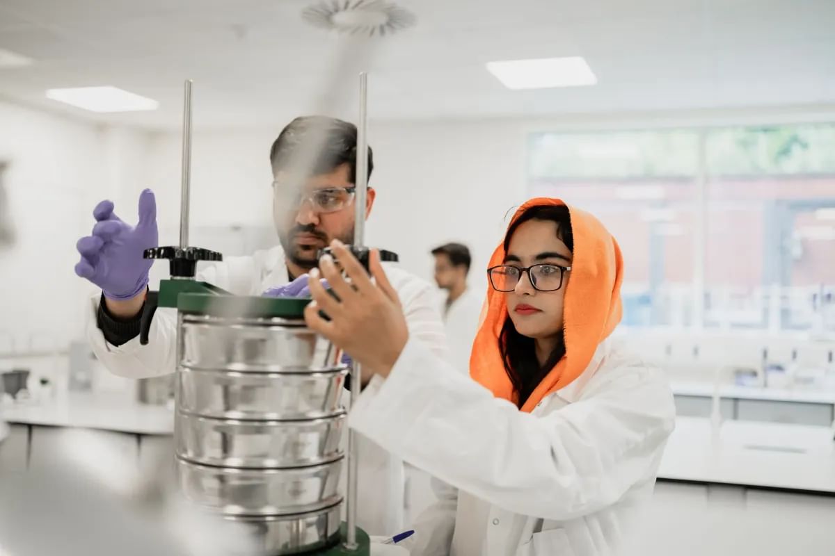 Two students working together in a lab, wearing white lab coats
