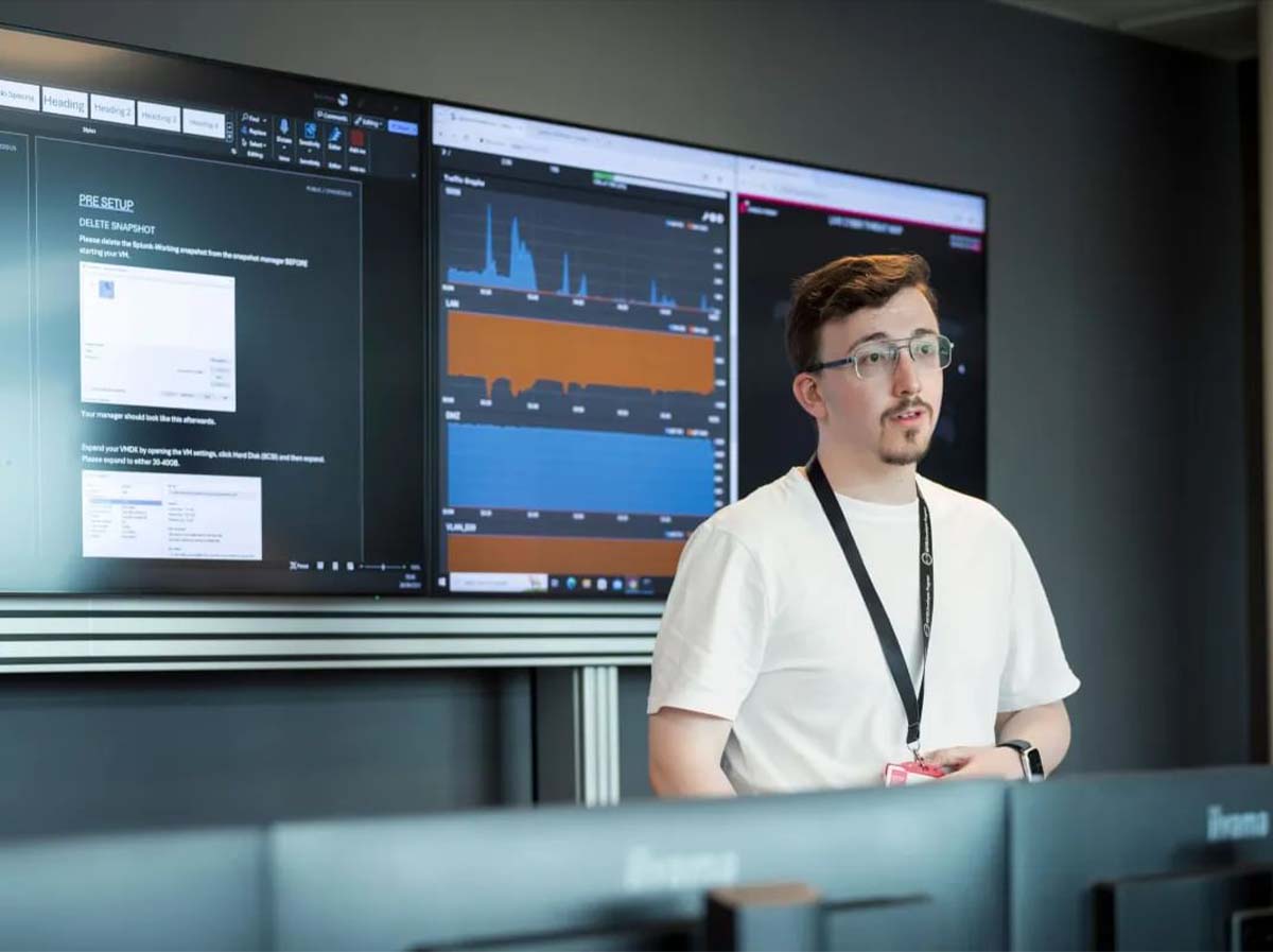 A man presenting in front of a screen that has cyber security information on it.