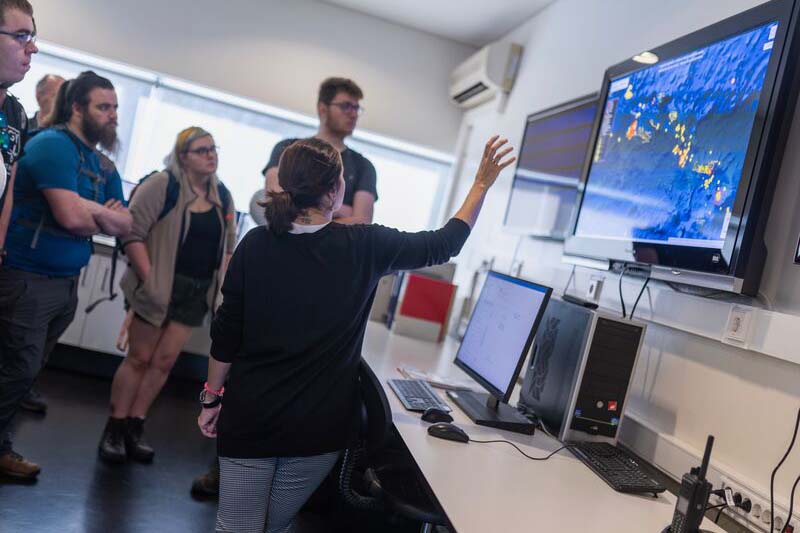 Students are looking at a screen displaying environmental information with a lecturer stood pointing at the information.