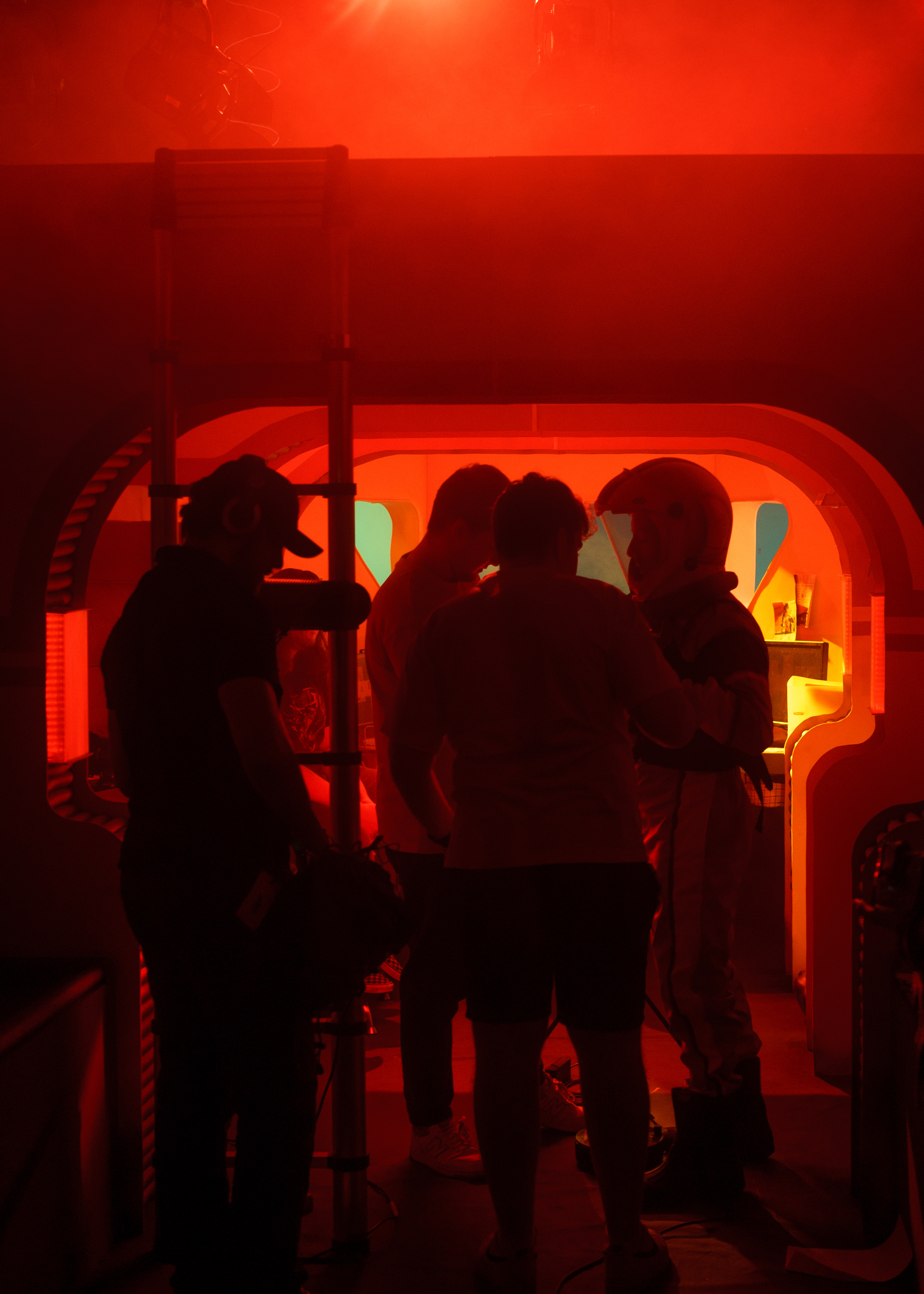 Film students filming on set. The lighting is red and a person is dressed as an astronaut.