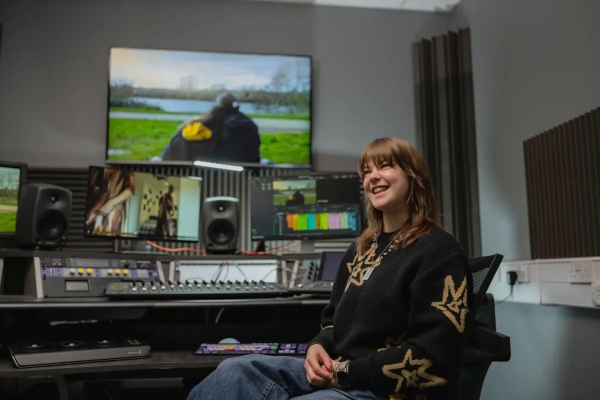 Student, Daisy, is sat in a recording studio and smiling.