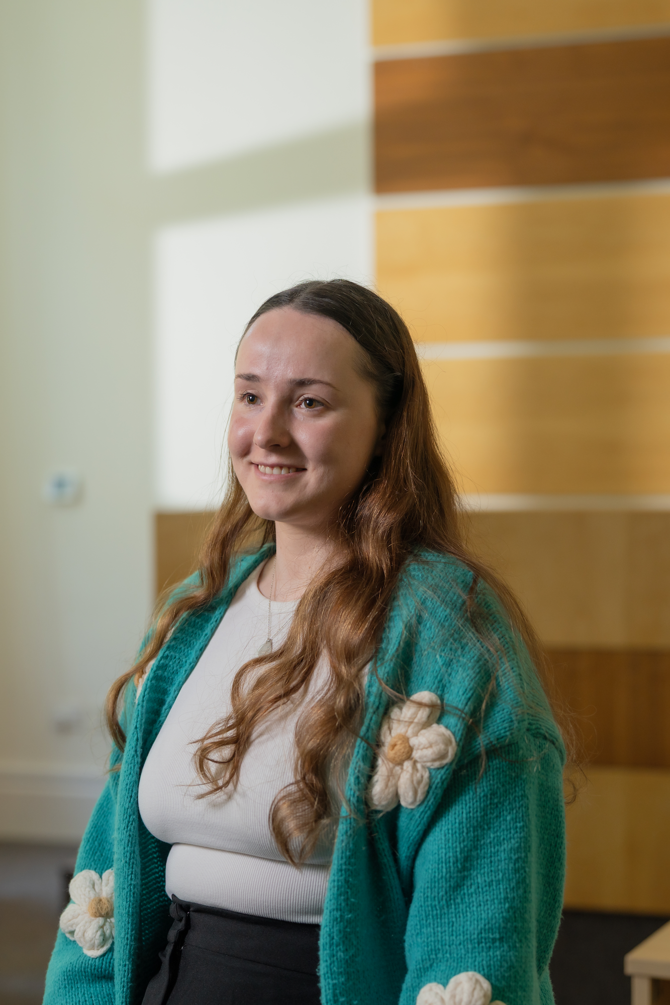 Postgraduate student Keihanah Joseph-Horne smiles at the camera while wearing a knitted turquoise cardigan with daisies on it inside the moot courtroom
