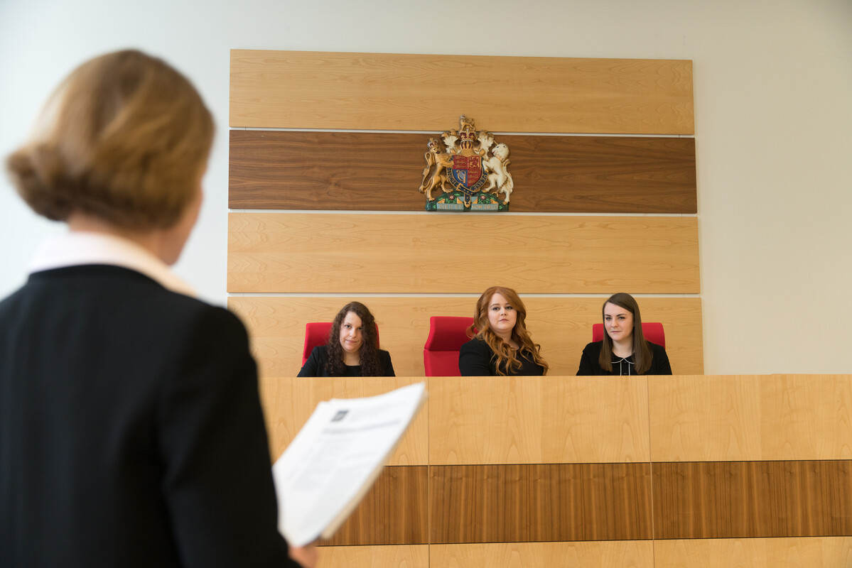 three students have taken seats in the moot court stand, they are listening to a statement being presented.