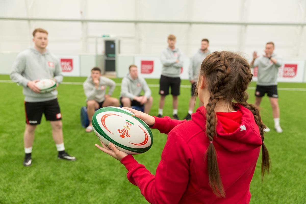Female rugby student holding a ball as other students observe