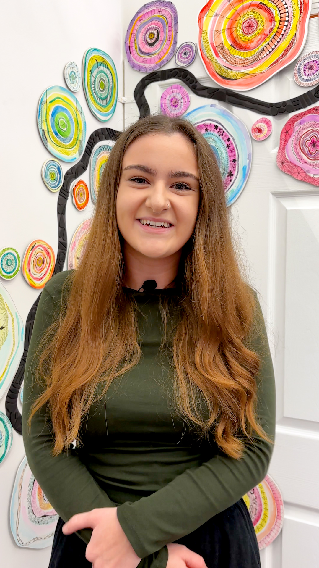A Creative and Therapeutic Arts student smiling at the camera, surrounded by colourful artwork