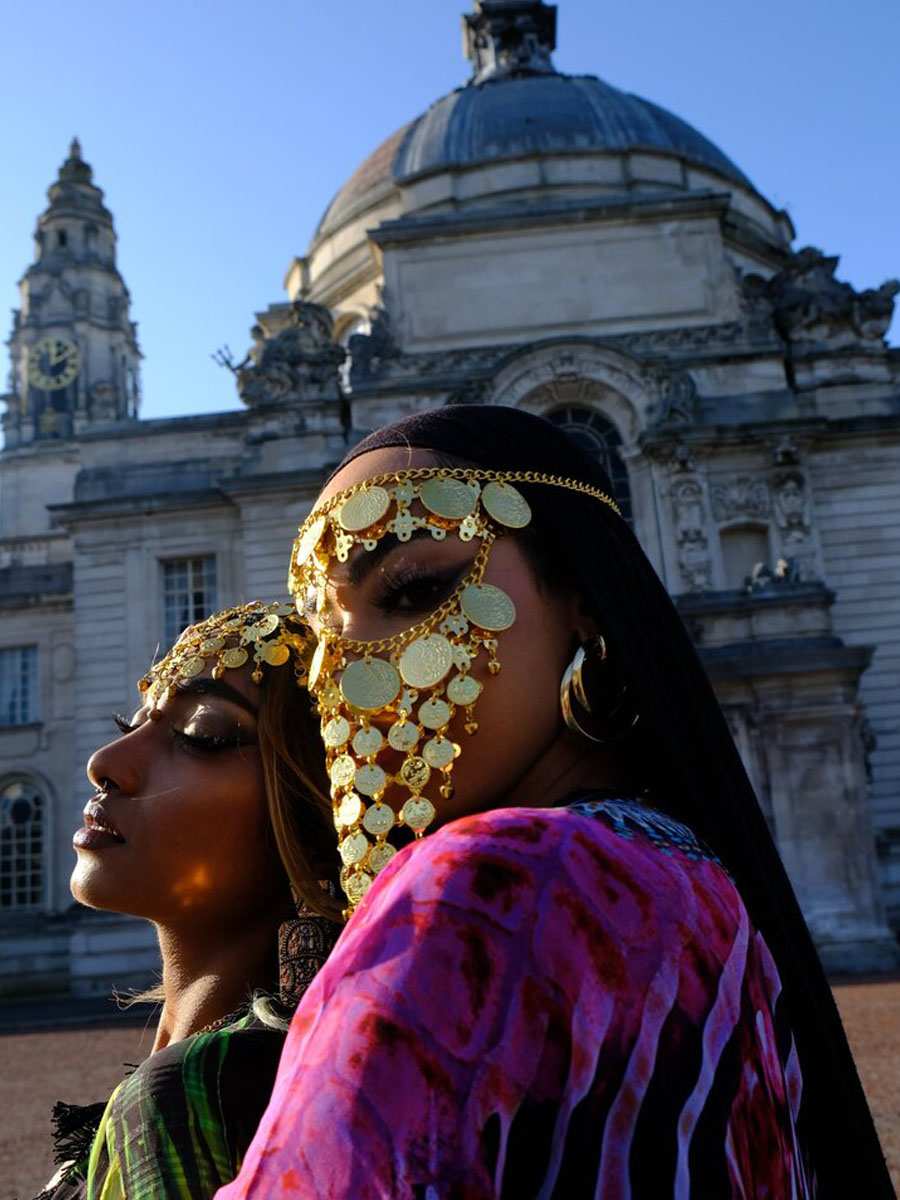 Two models of the global majority pose for a camera while wearing a face veil made of metal in front of Cardiff City Hall