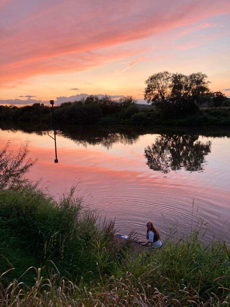 Lucy smiling at camera before going paddleboarding, with a sunrise in the distance