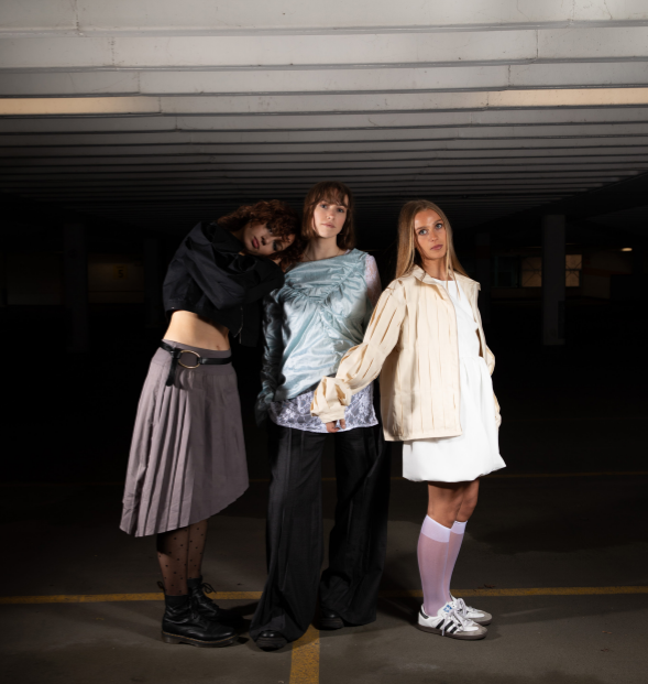 Three models stood back to back in a darkly lit carpark wearing stylised outfits
