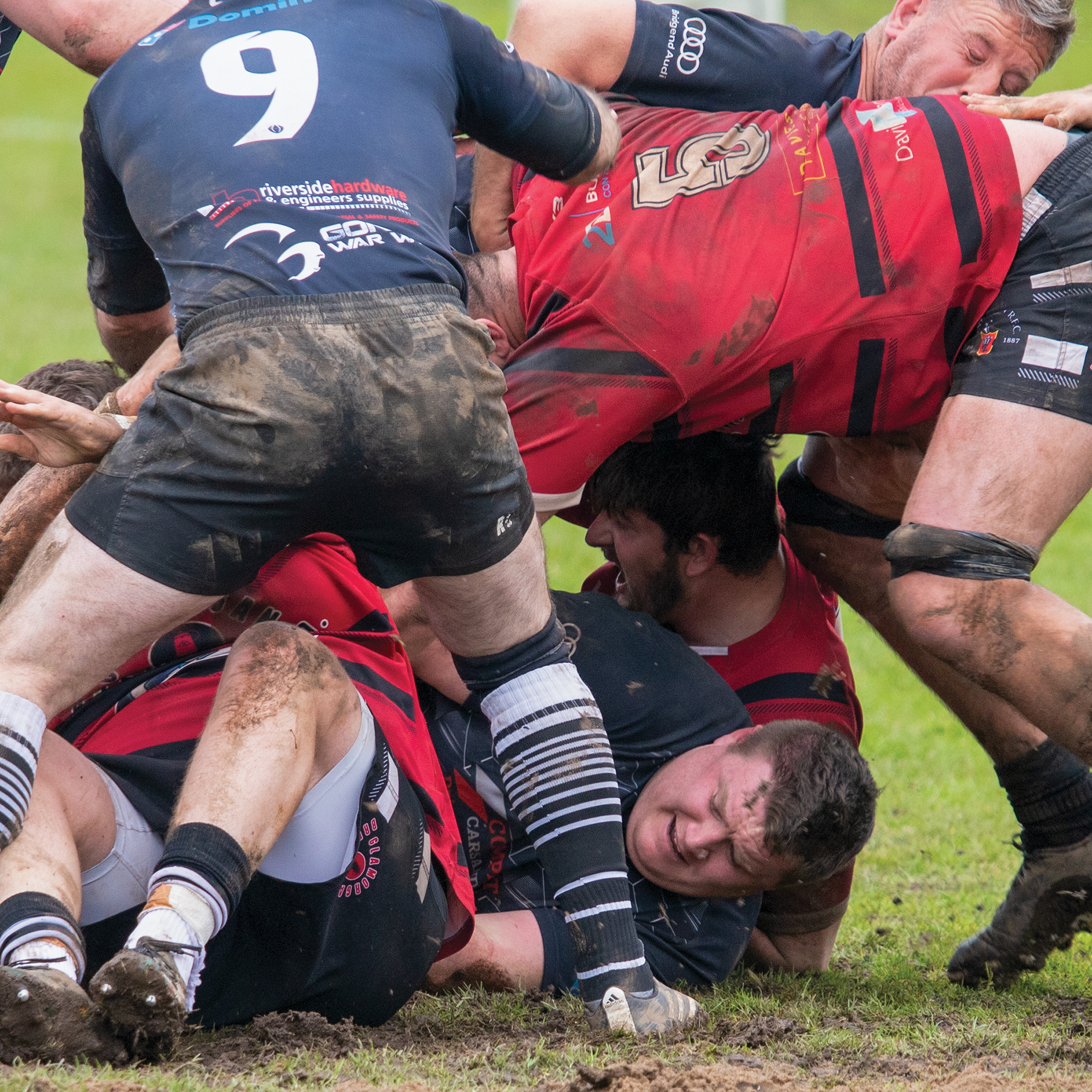 A scrum between two muddy rugby teams, one in red and the other in navy