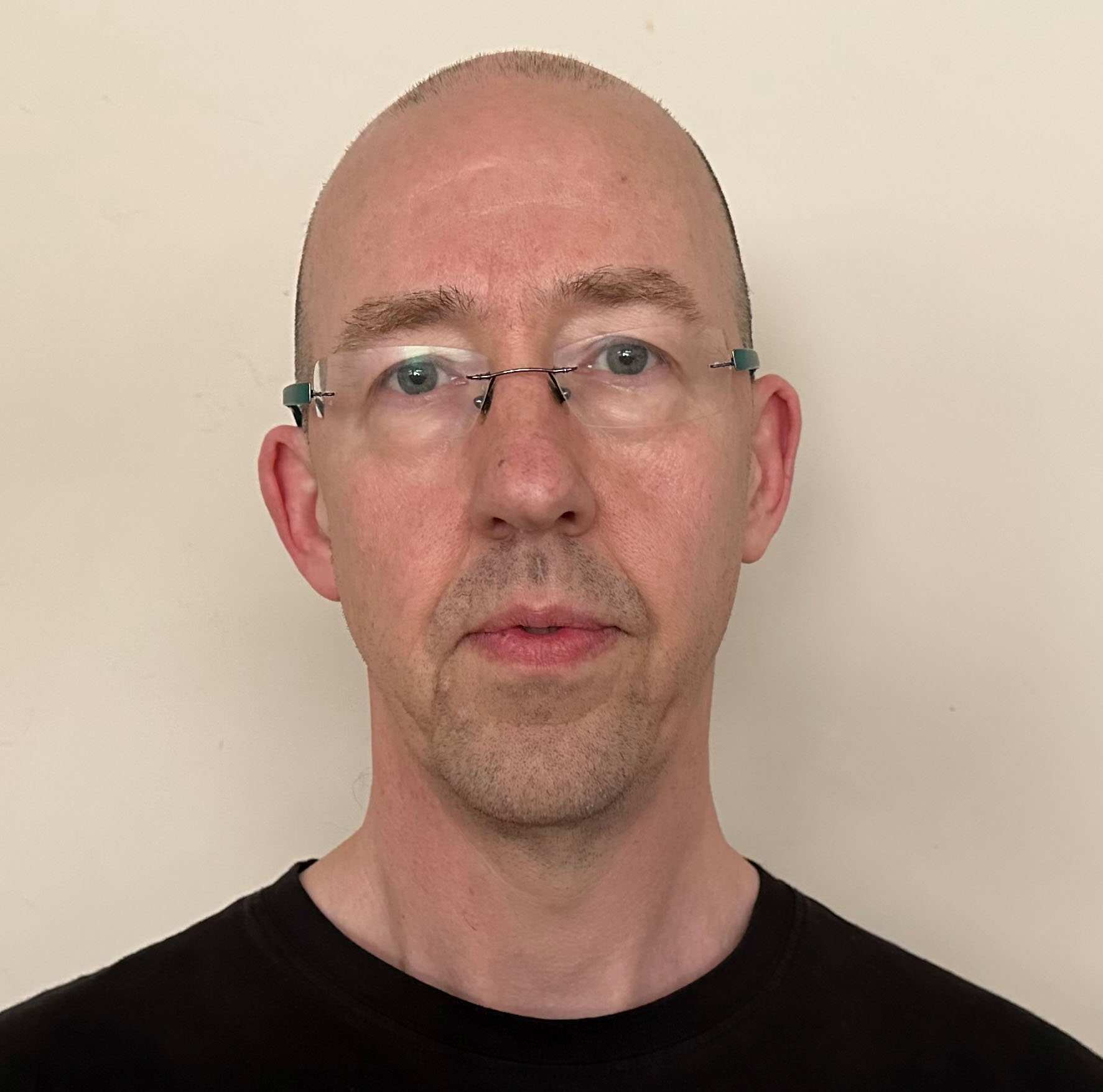 Associate Professor Mark Davies looks at the camera in front of a cream wall