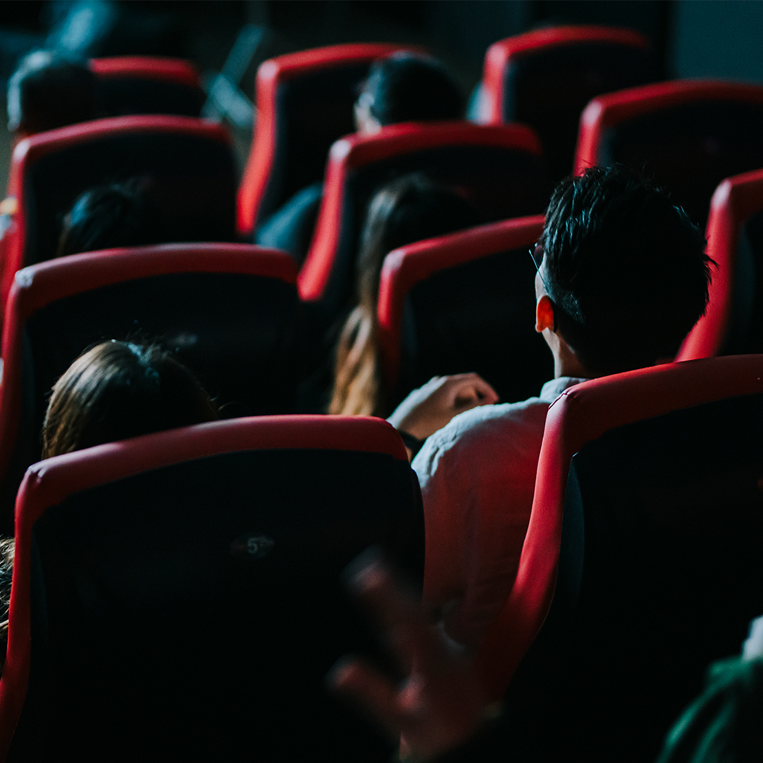 Two people sat in a dark cinema screen watching a movie