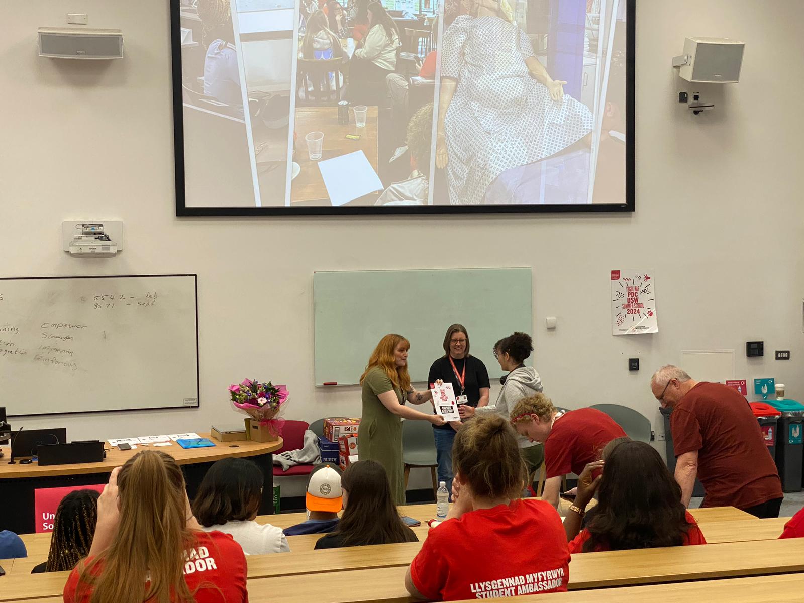 lecture theatre filled with pupils wearing red jumpers receiving certificates