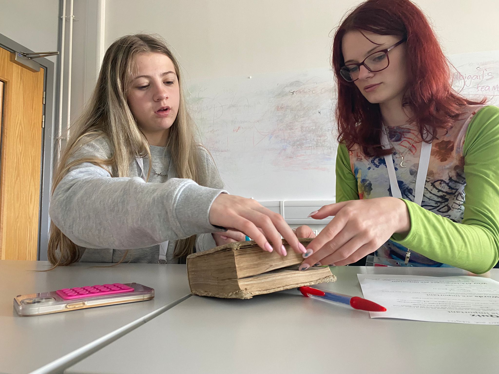 two females sitting at a desk flicking through pages in a book