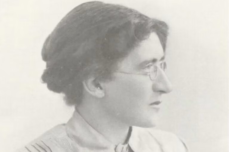 An old photographic portrait of a woman. She is wearing glasses and has long hair that is pinned up.